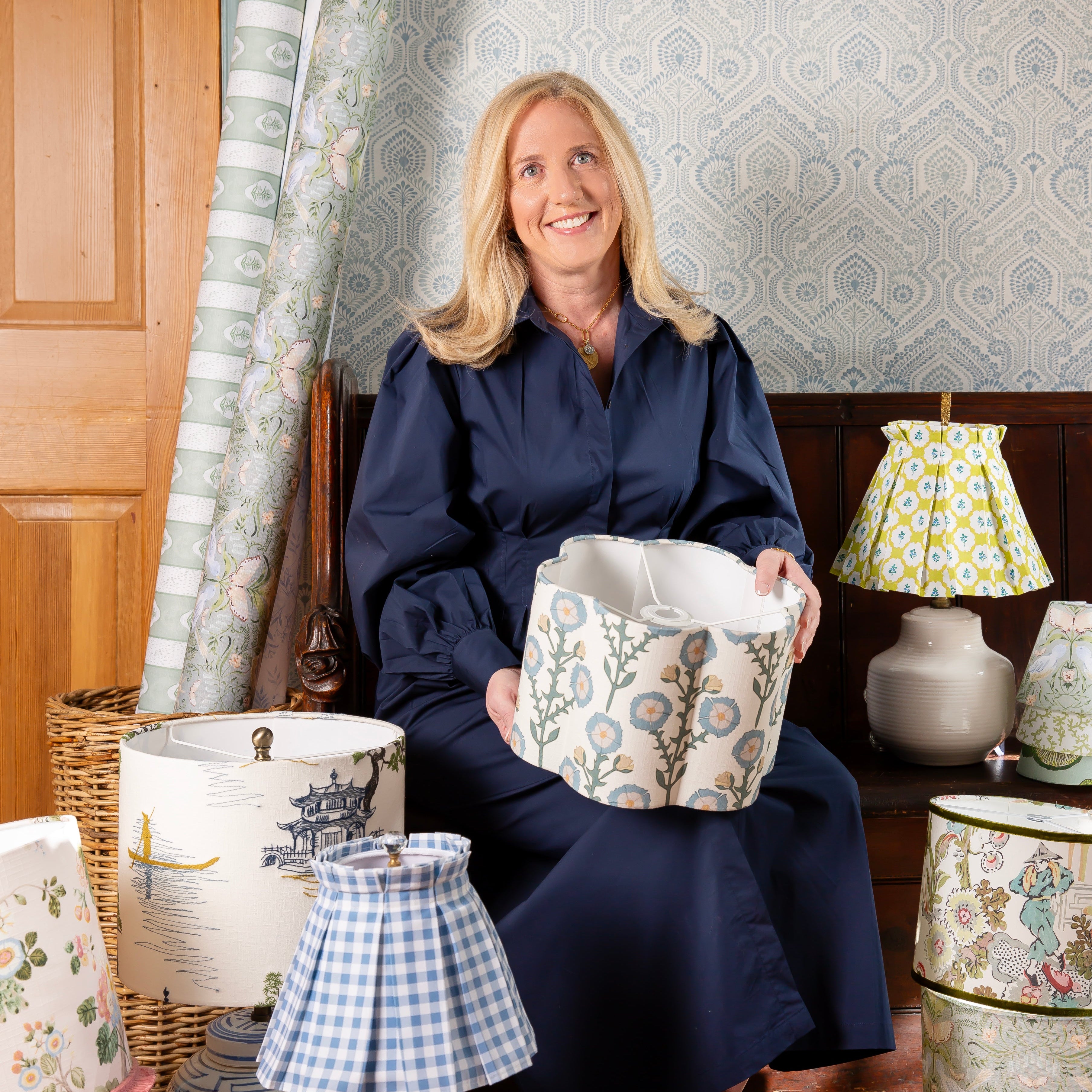 Woman sitting with decorative items including lamps and fabric samples in a home setting.