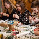 Group of women sitting around a table with various items, including scissors and small containers.